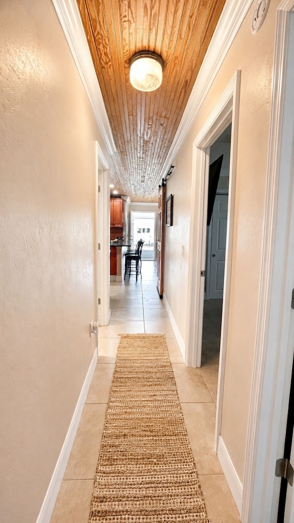 A hallway with a wooden ceiling, a kitchen area in the background, and a door on the right.