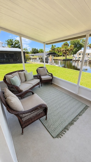 A covered patio area with wicker furniture and a view of a water body.