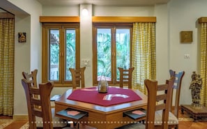 A dining area with a wooden table, chairs, and a view through large windows. - Luxury Hillside Estate with Heated Indoor Pool (Lonavala)