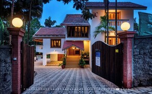 A two-story house with a paved entrance, a staircase leading to the main door, and a gated driveway. - Luxury Hillside Estate with Heated Indoor Pool (Lonavala)
