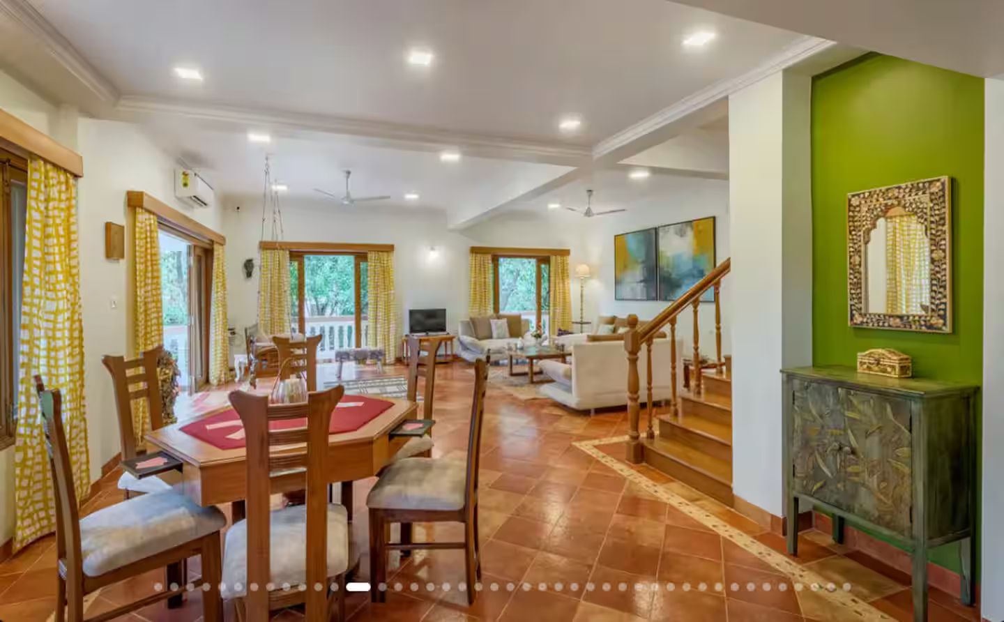 A spacious dining area with a high ceiling, a staircase, and a green accent wall.