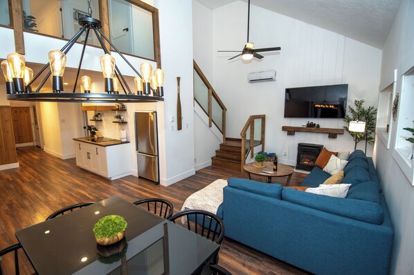 A modern living space with a dining area, kitchen, and a cozy seating area with a fireplace. - Lakefront Retreat/5 BR/Games Room/Beach/Karaoke (Canning)