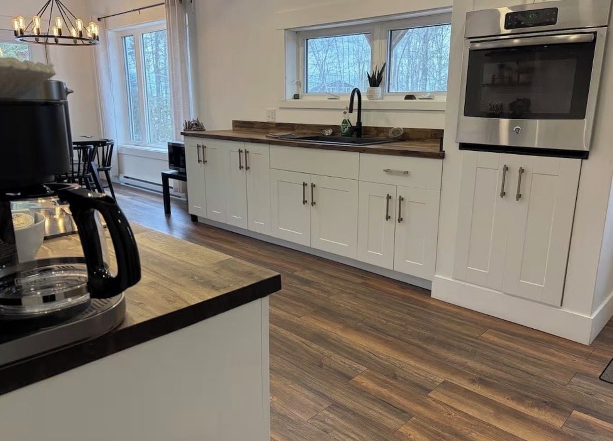 A modern kitchen with white cabinets, a stainless steel oven, and a black coffee machine.
