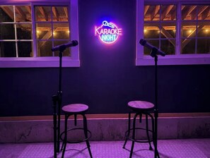 A karaoke setup with two stools and microphones, a neon sign reading 'Karaoke Night,' and windows with warm lighting. - Lakefront Retreat/5 BR/Games Room/Beach/Karaoke (Canning)
