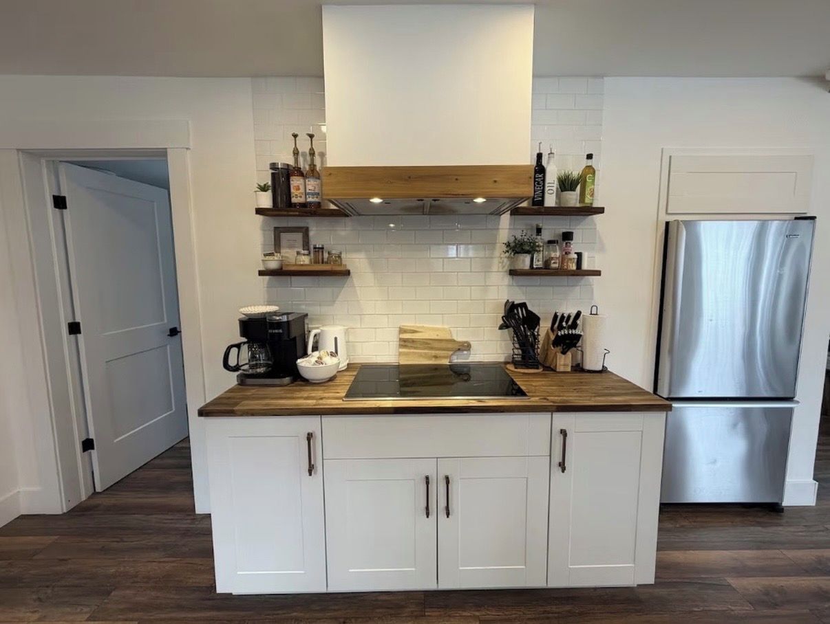 A modern kitchen with white cabinetry, a stainless steel refrigerator, and wooden countertops.
