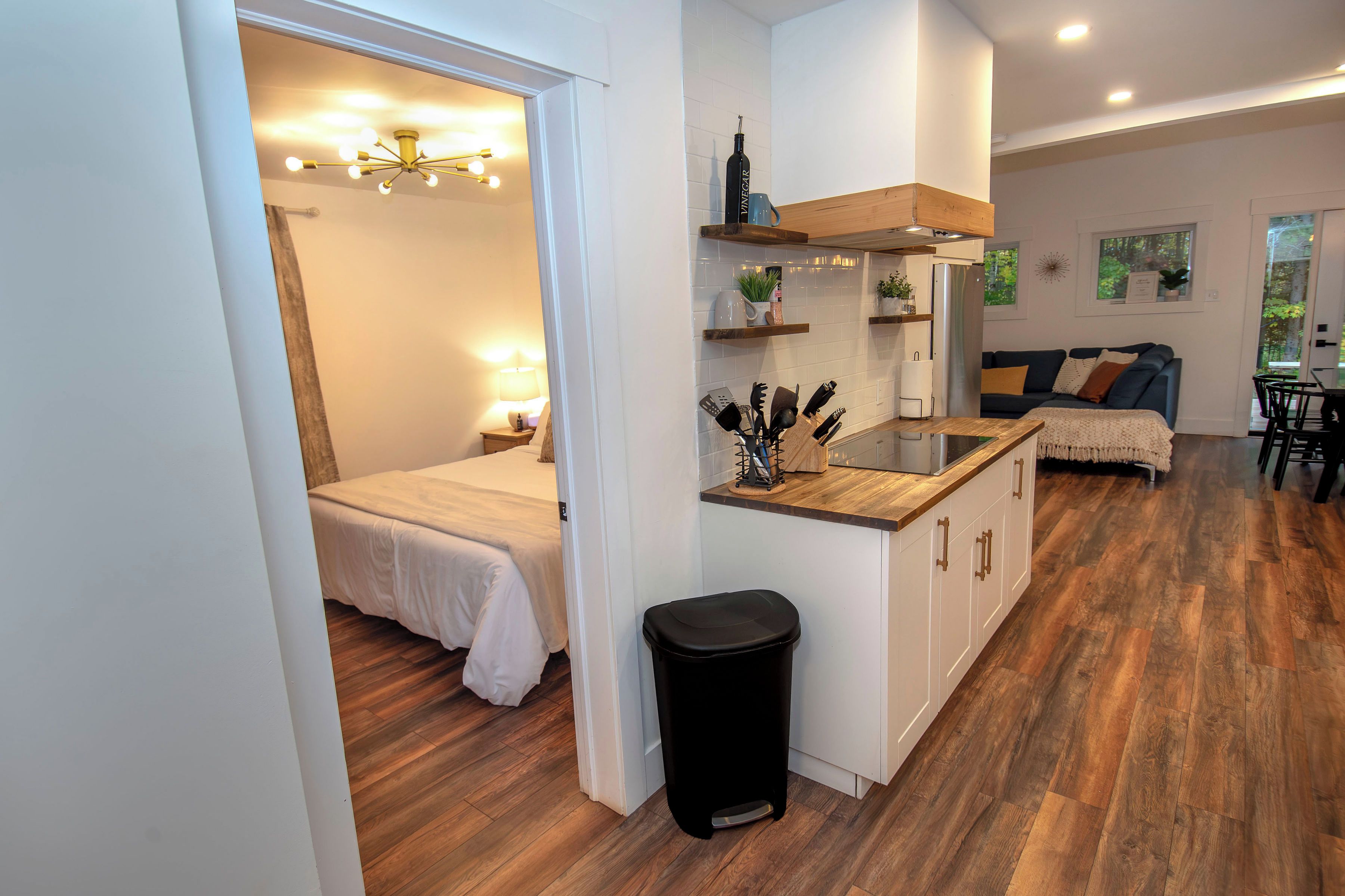 A modern kitchen with wooden cabinets, a countertop, and a sink. There is a dining area with a table and chairs, and a living room with a sofa and a coffee table.