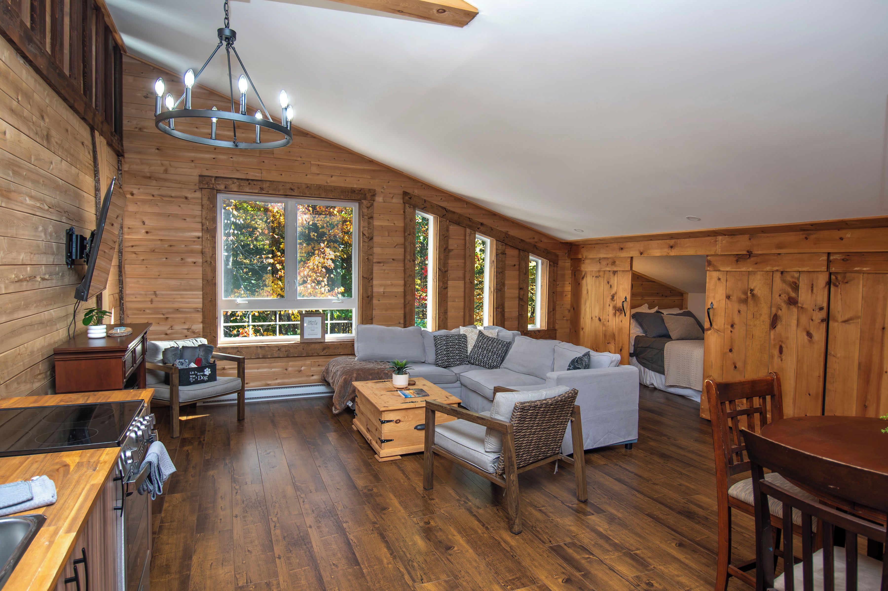 A cozy cabin interior with a wooden interior, a sofa set, a dining table, and a kitchen area.
