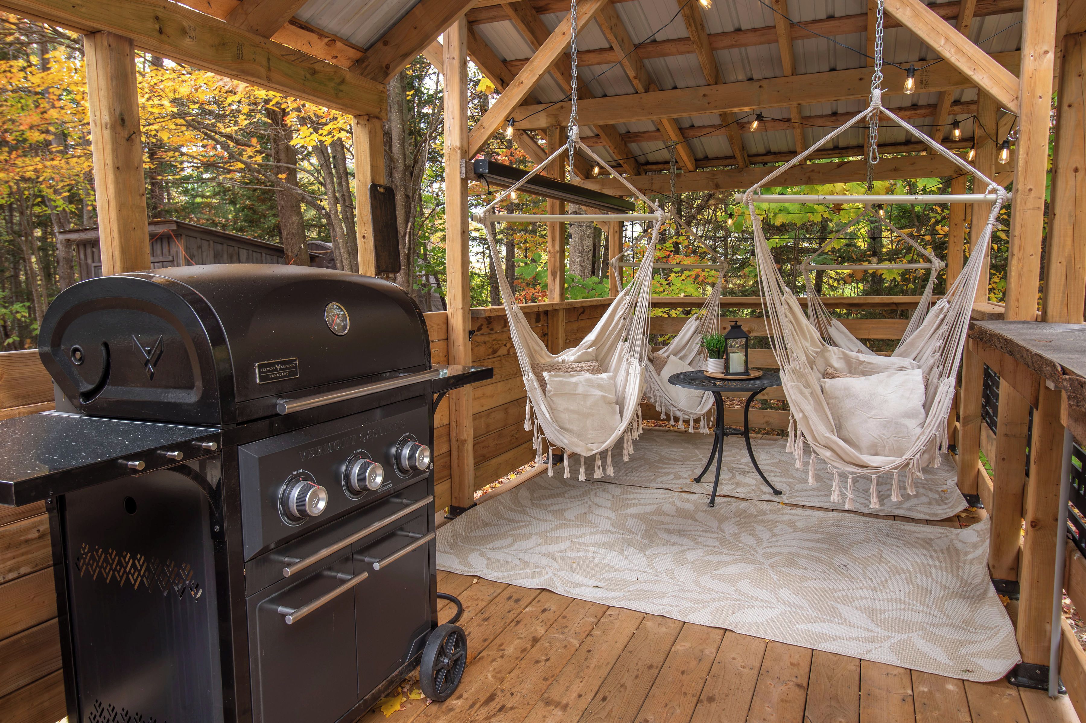 A wooden deck with a black grill, two white hammocks, and a patterned rug.