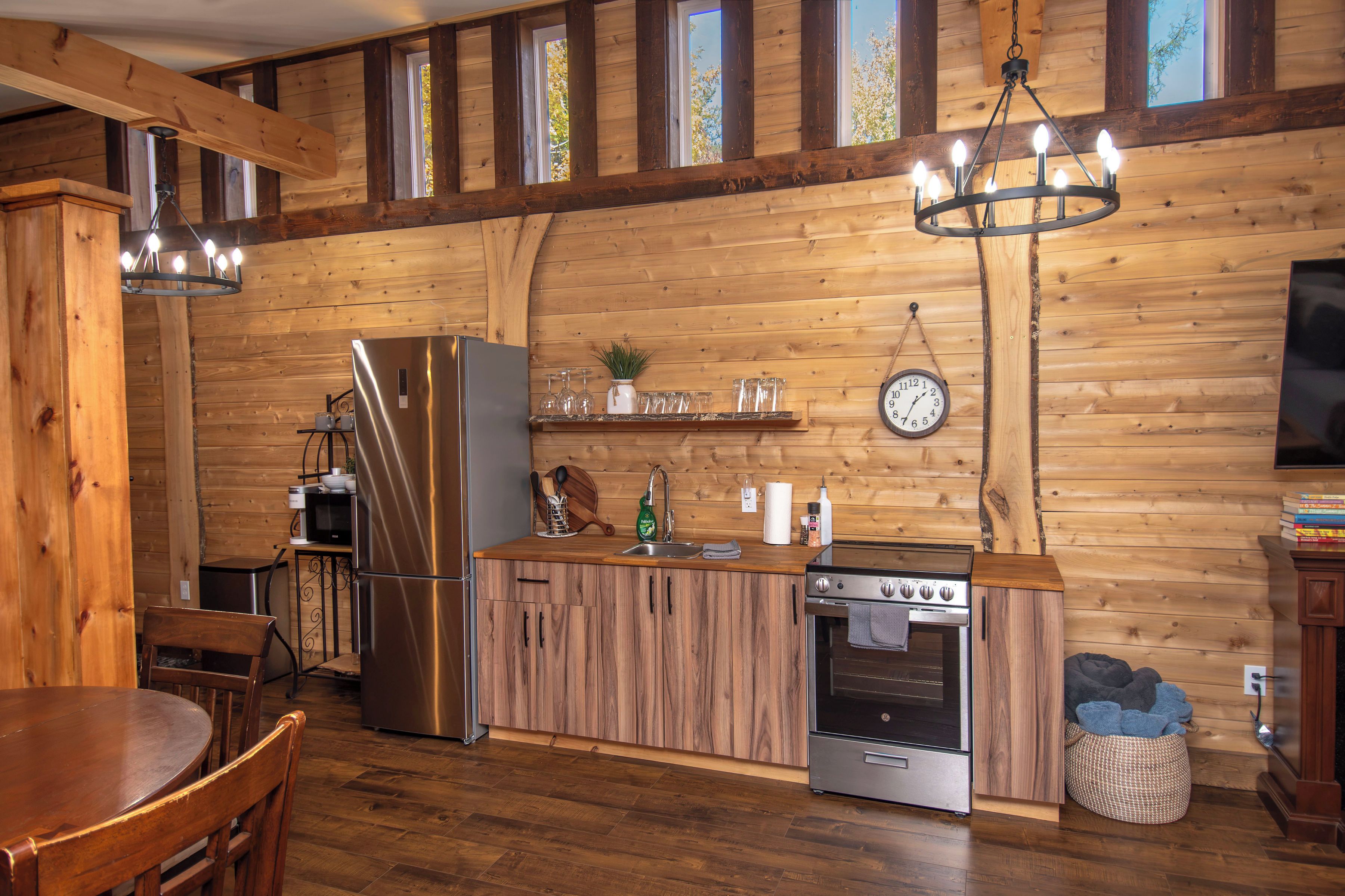 A wooden interior with a kitchen area featuring a refrigerator, microwave, stove, and wooden cabinets.
