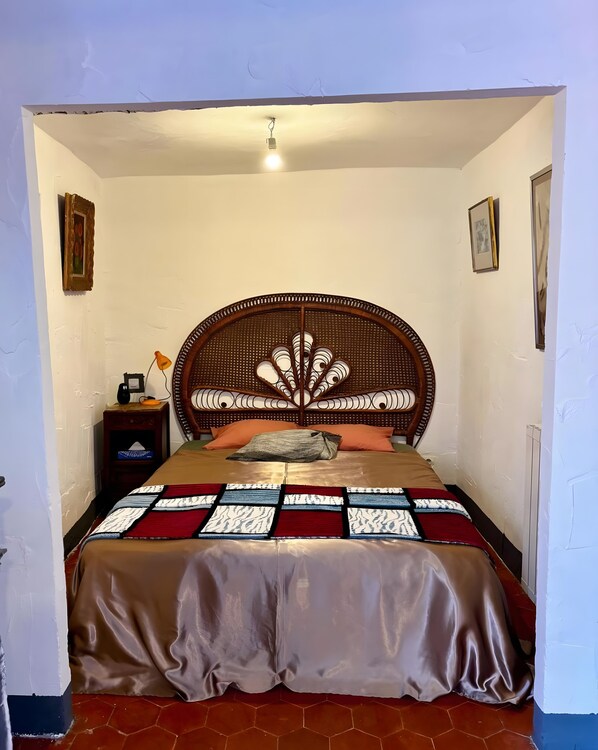 A bed with a rattan headboard, a quilt, and a nightstand with a lamp.
