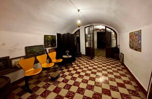 A room with a checkered floor, two orange chairs, a table with a vase, and a hanging light fixture.