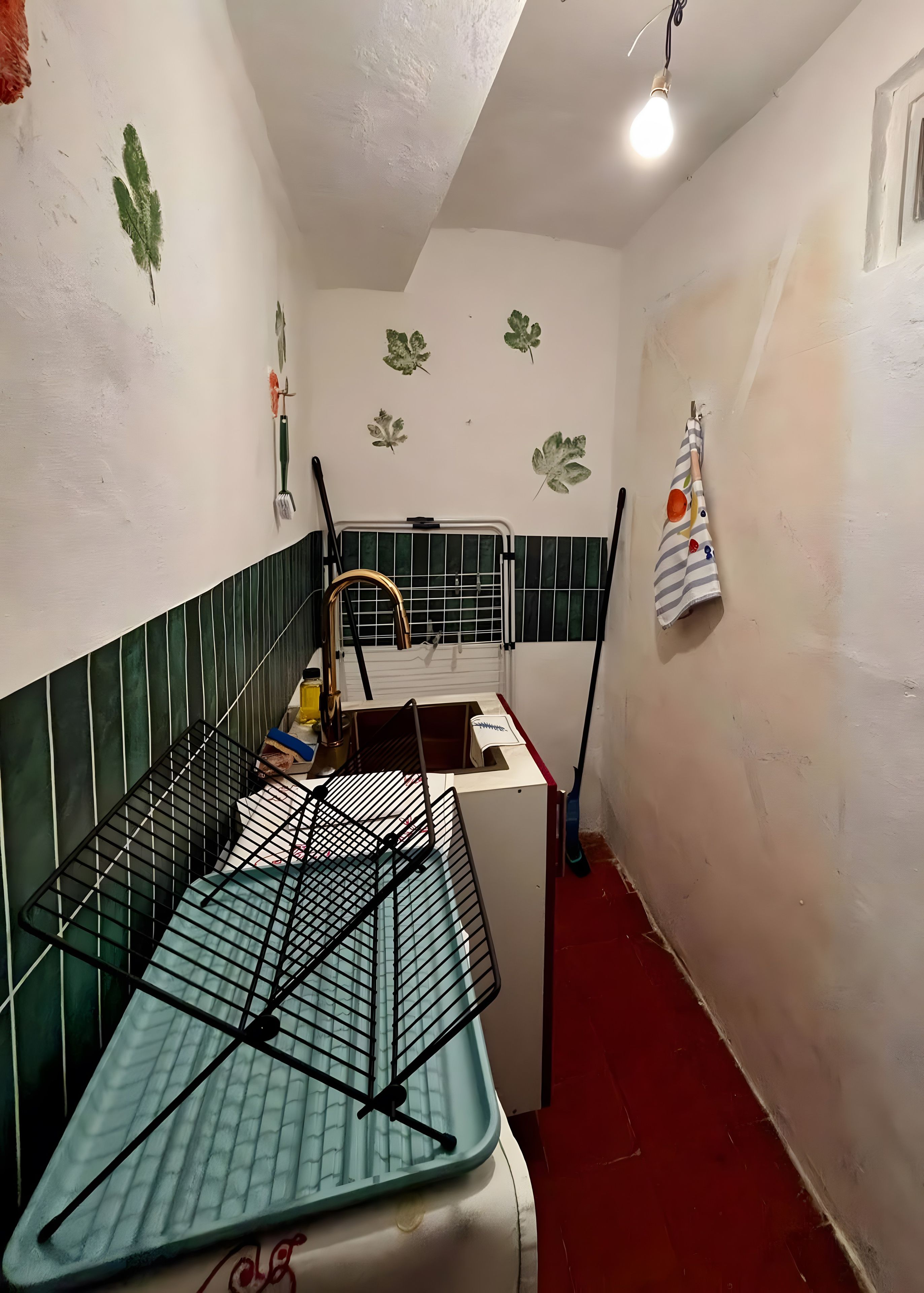 Een kleine kamer met een metalen rek, een witte kast en een bezem die tegen de muur staat.