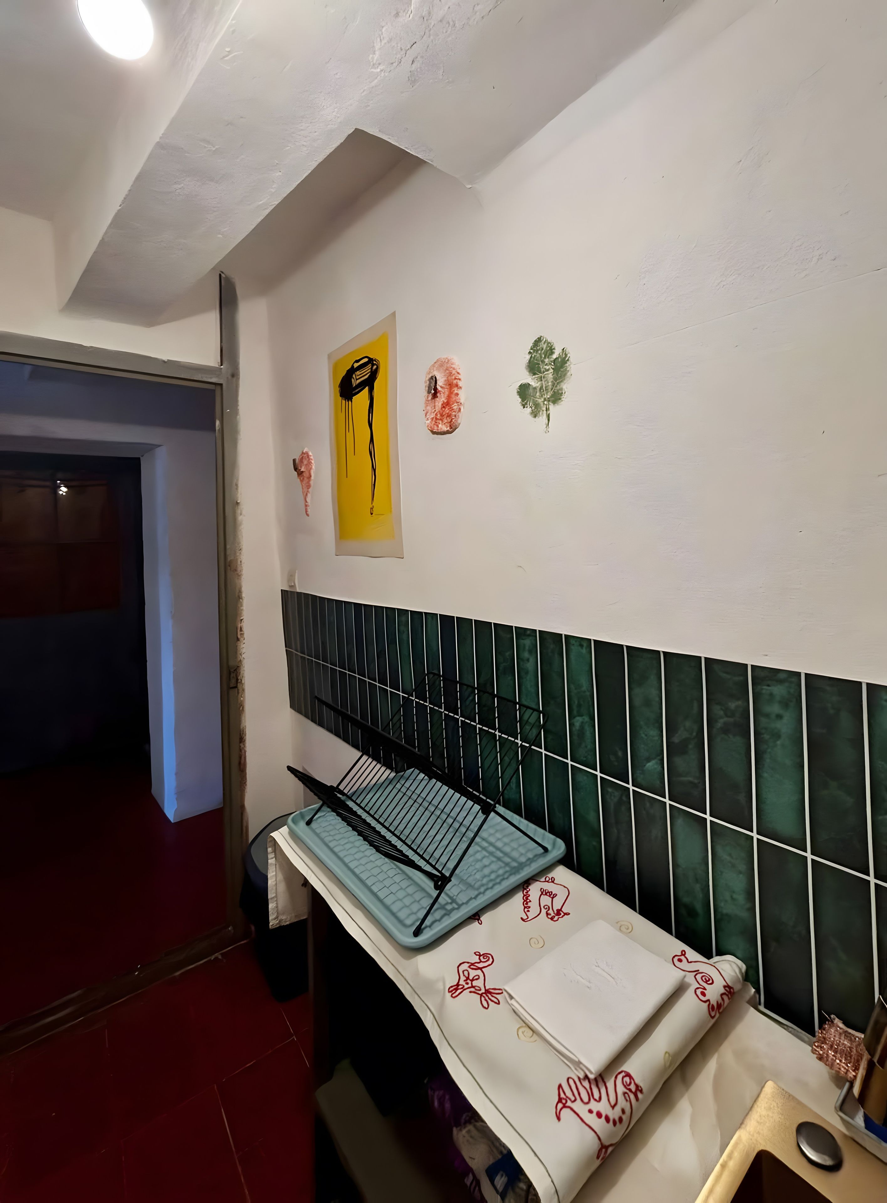A kitchen with a tiled backsplash, a drying rack, and a wall-mounted light fixture.