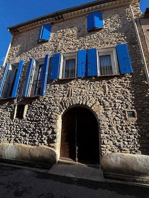 Un edificio in pietra con un portale ad arco centrale e diverse finestre con persiane blu.