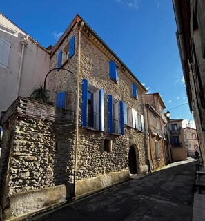 Una calle estrecha con edificios de piedra, uno con una entrada abovedada y contraventanas azules.