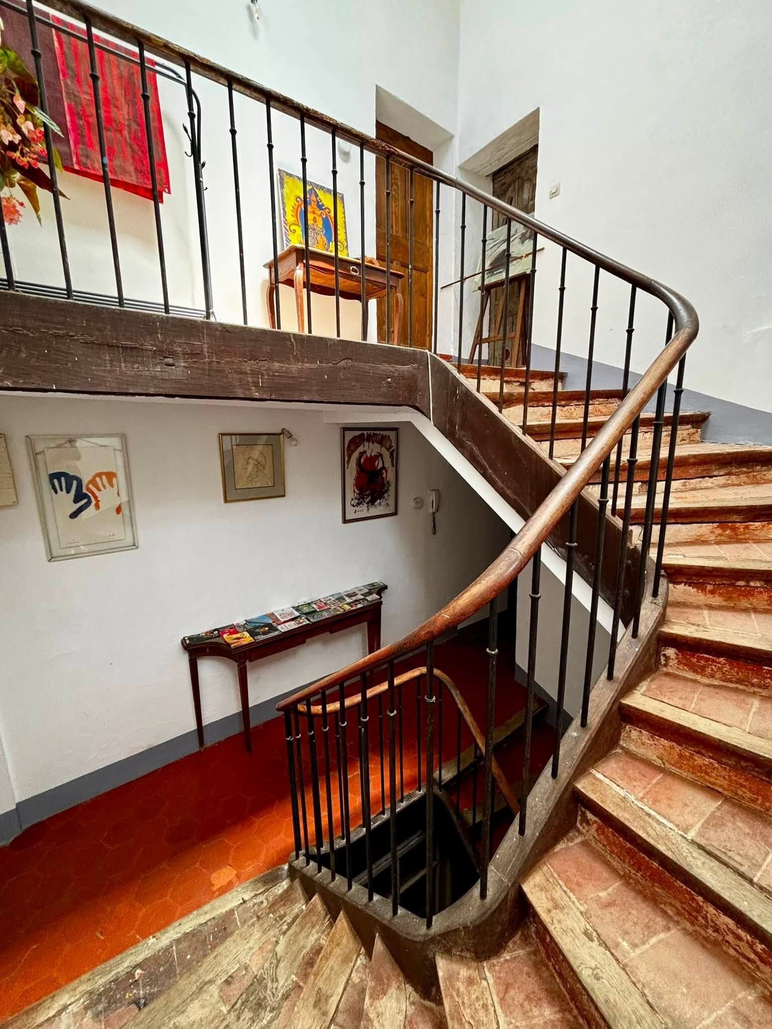 A spiral staircase with a wooden handrail and black balusters, leading to an upper floor.