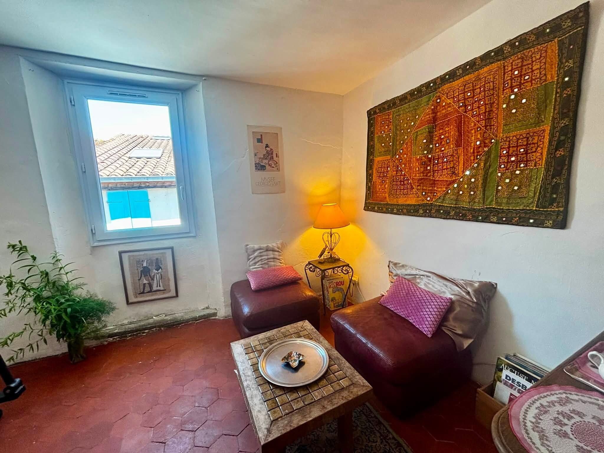 Ein Wohnzimmer mit Fenster, Lampe, einer Couch, einem kleinen Tisch und einer Wanddekoration.