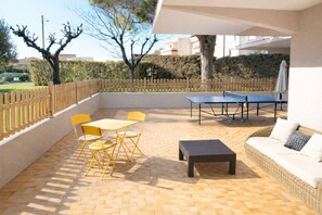 An outdoor patio with a ping pong table, yellow chairs, a small table, and a wicker sofa. - Cozy 2-room apartment on the first floor in a quiet complex with a pool (Antibes)