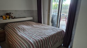 A bedroom with a bed, a window with curtains, and a shelf with stuffed toys. - Cozy 2-room apartment on the first floor in a quiet complex with a pool (Antibes)