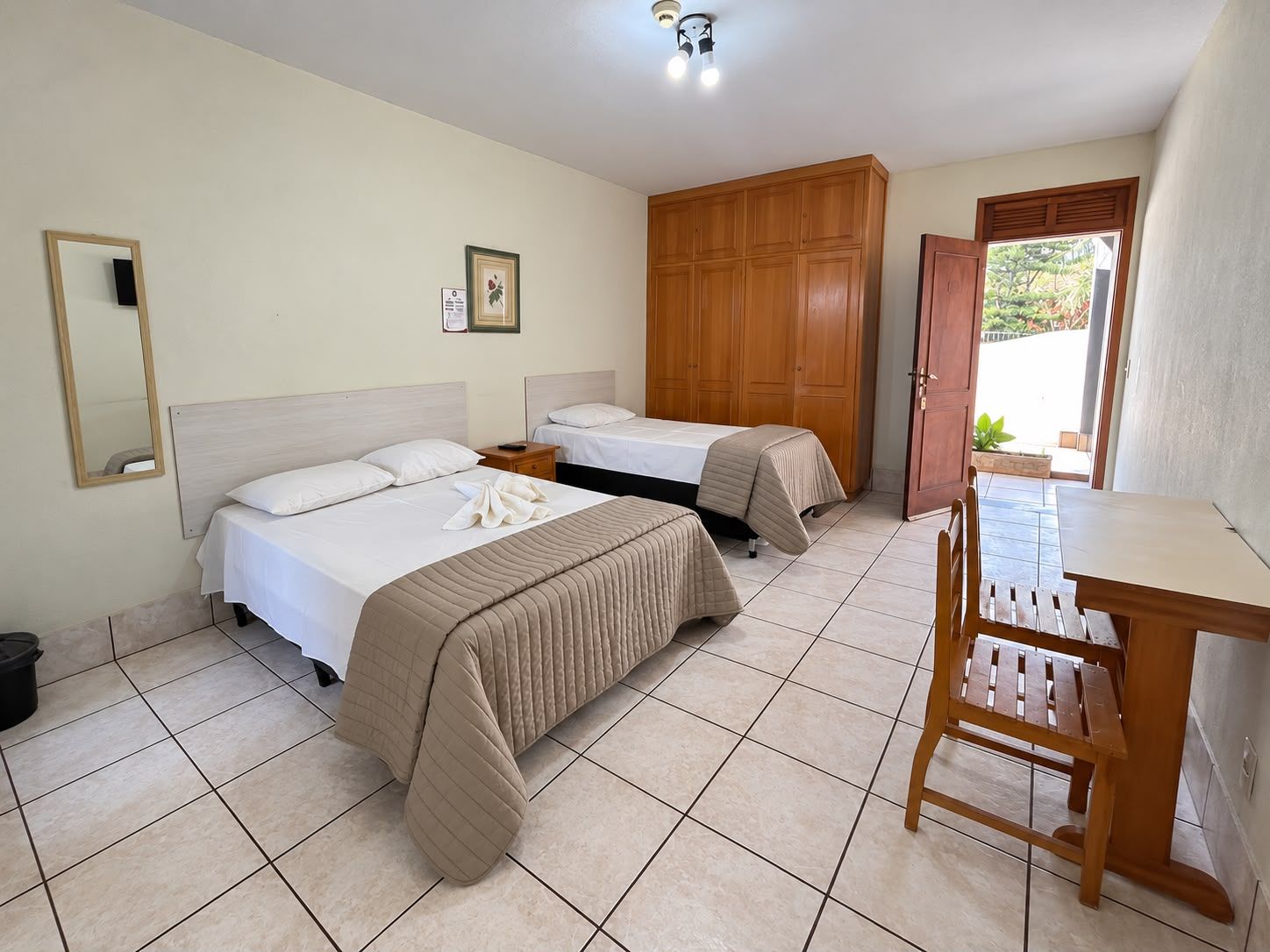 A hotel room with two beds, a wooden wardrobe, a small table, and a chair.