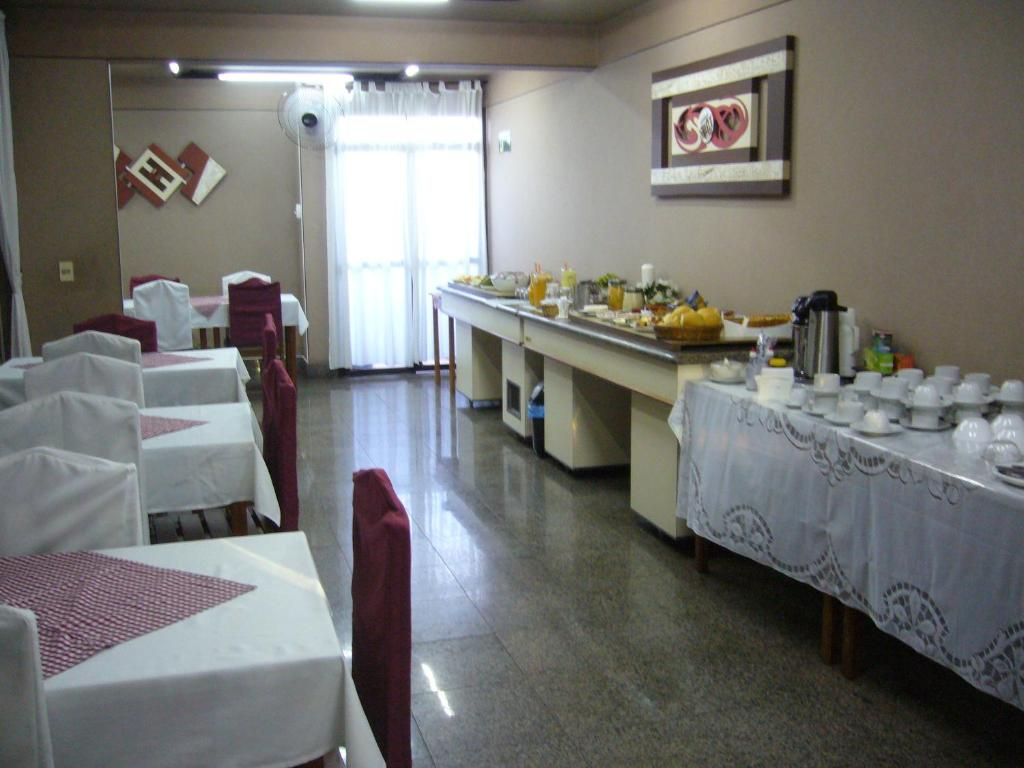Uma sala de jantar com mesas preparadas para refeição, um buffet com comida e bebidas, e um relógio fixado na parede.