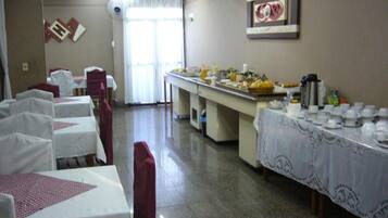 Uma sala de jantar com mesas preparadas para refeição, um buffet com comida e bebidas, e um relógio fixado na parede.