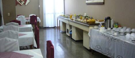 Un espace repas avec des tables dressées pour le service, un buffet proposant des plats et des boissons, et une horloge fixée au mur.