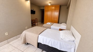 Quarto de hotel com duas camas, um guarda-roupa de madeira, uma escrivaninha com cadeira e uma televisão.