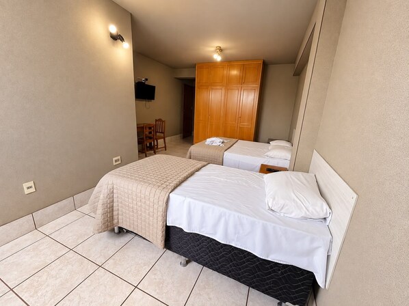 A hotel room with two beds, a wooden wardrobe, a desk with a chair, and a television.
