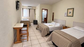 Ein Hotelzimmer mit zwei Betten, einem Schreibtisch, einem Stuhl, einem kleinen Tisch, einem Spiegel, einem Bilderrahmen und einer Wandleuchte.