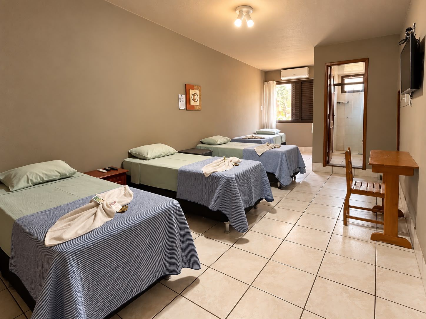 A hotel room with four beds, a wooden chair, a small table, and a TV mounted on the wall.