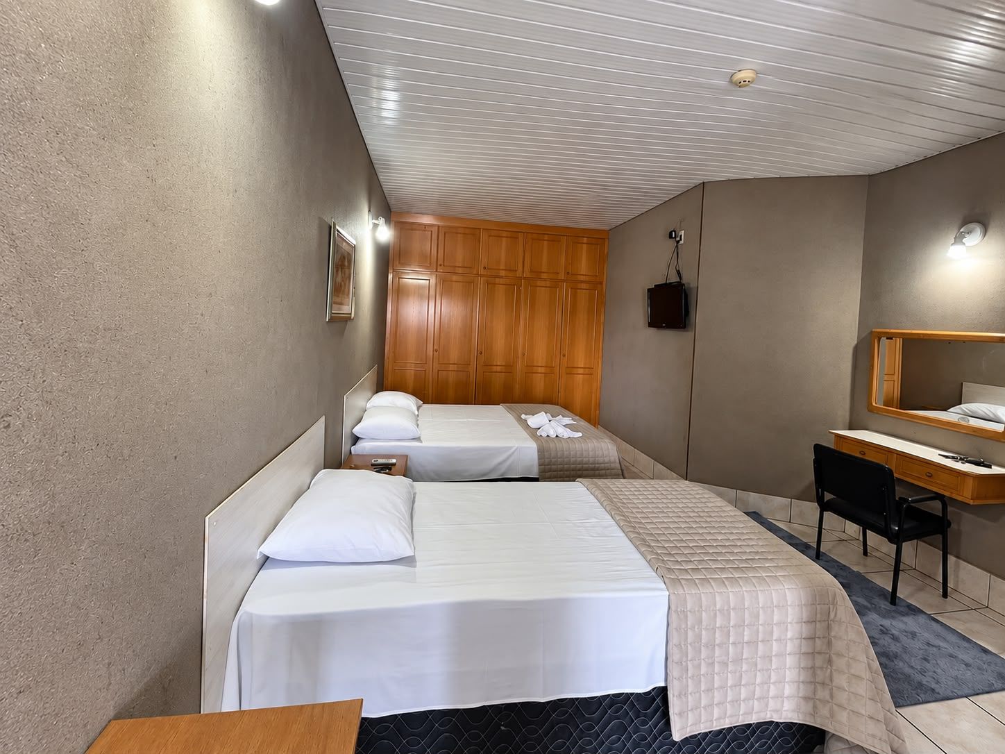 A hotel room with two beds, a desk, a chair, a wardrobe, and a mirror.