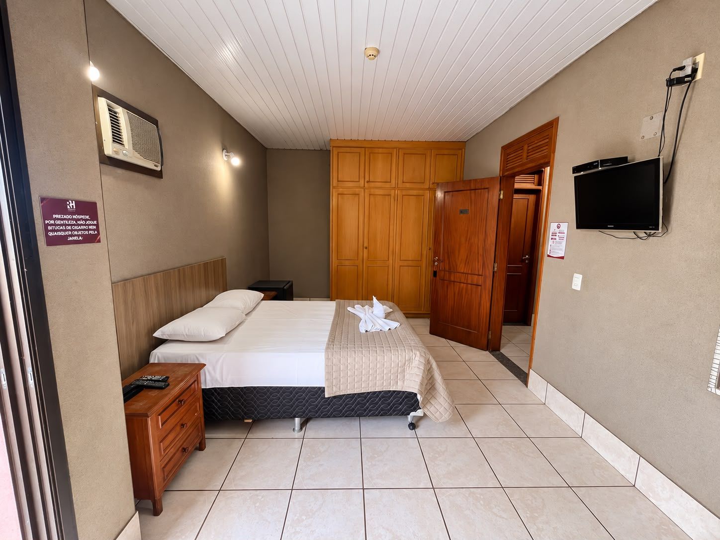 Una habitación de hotel con cama, armario de madera, televisor y mesita de noche.