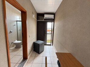 A narrow hallway with a toilet, a small black cabinet, and a window leading to a balcony.