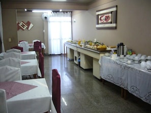 A dining area with tables set for a meal, a buffet line with food and beverages, and a wall-mounted clock.