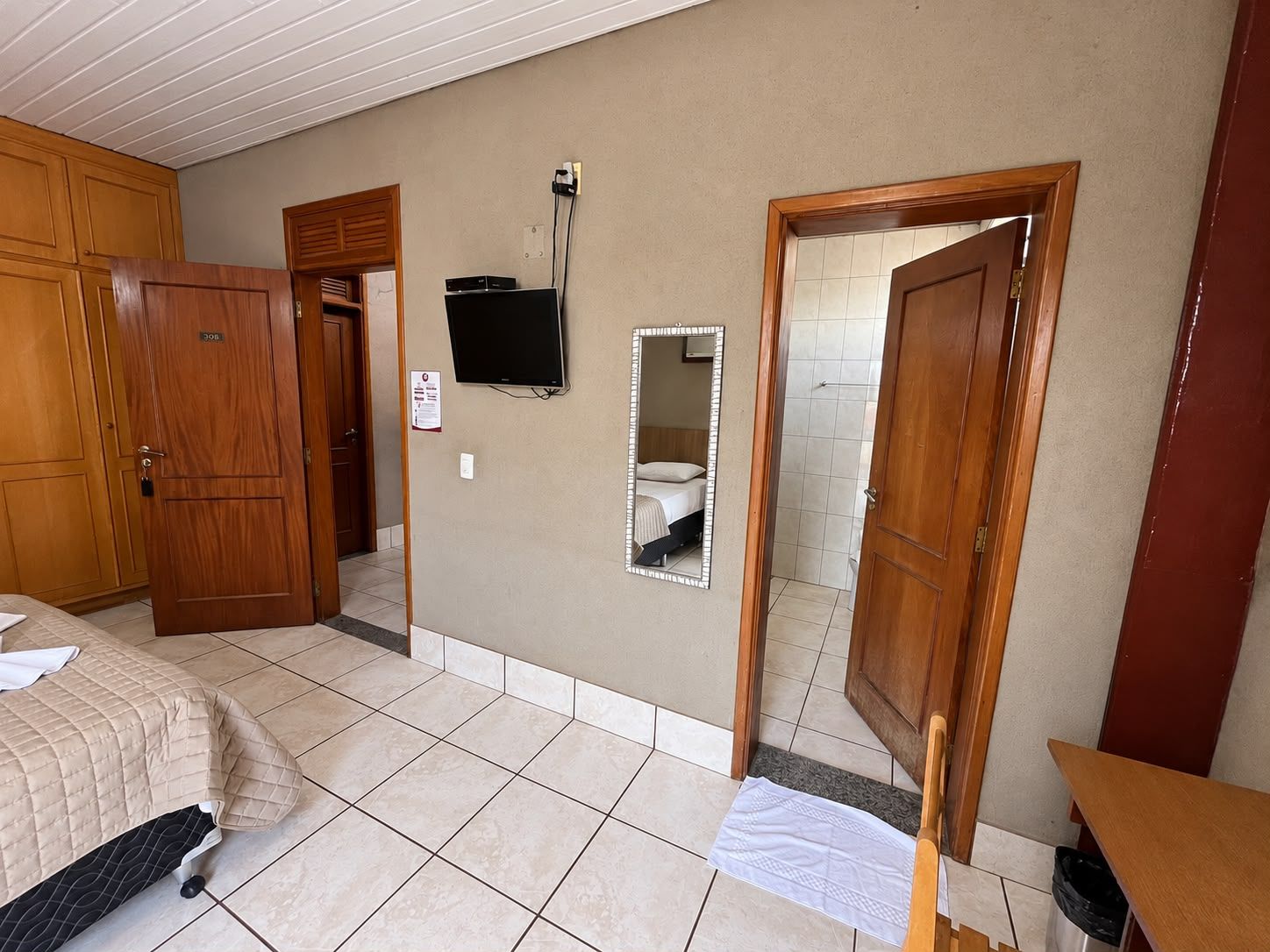 Una habitación de hotel con una cama, televisor, espejo y una puerta que da a otra habitación.