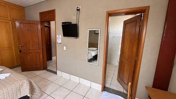 Una habitación de hotel con una cama, televisor, espejo y una puerta que da a otra habitación.