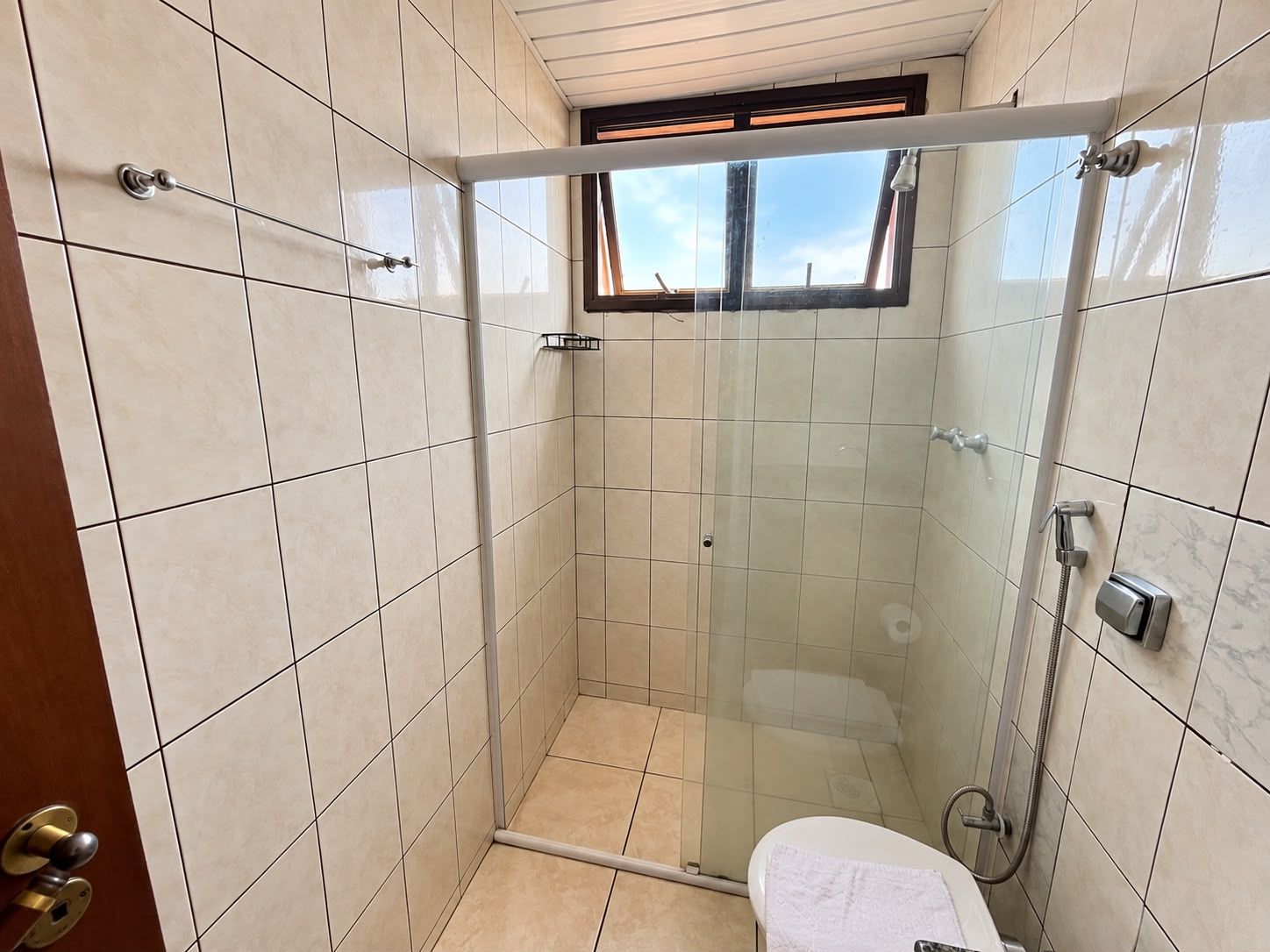 A walk-in shower with a glass door, tiled walls, a window, and a toilet.