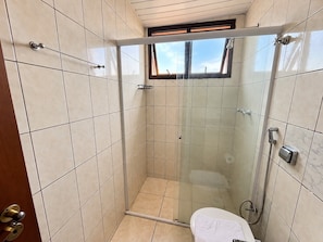 A walk-in shower with a glass door, tiled walls, a window, and a toilet.