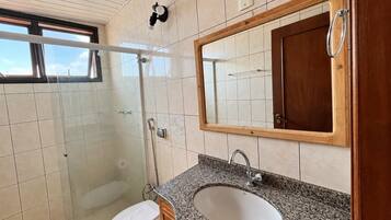 A bathroom with a shower, toilet, sink, and a large mirror.