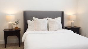 Een bed met wit beddengoed, twee nachtkastjes met lampen en een potplant.