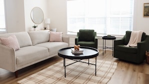 Een woonkamer met een bank, twee fauteuils, een salontafel en een groot raam met luxaflex.