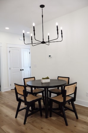 Un coin repas avec une table ronde, quatre chaises, un lustre noir et un thermostat fixé au mur.