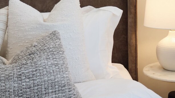 Een net opgemaakt bed met hoofdeinde, een lamp op een nachtkastje en een lijst met een afbeelding aan de muur.