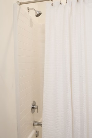 Un espace douche avec un mur recouvert de carreaux blancs, une pomme de douche et un rideau.