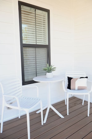 A white outdoor seating area with two chairs and a small table, a potted plant, and a window with blinds. - Rooftop view on Shipley (Cookeville)