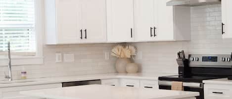 A modern kitchen with white cabinetry, a central island with stools, pendant lighting, and a stainless steel range hood.