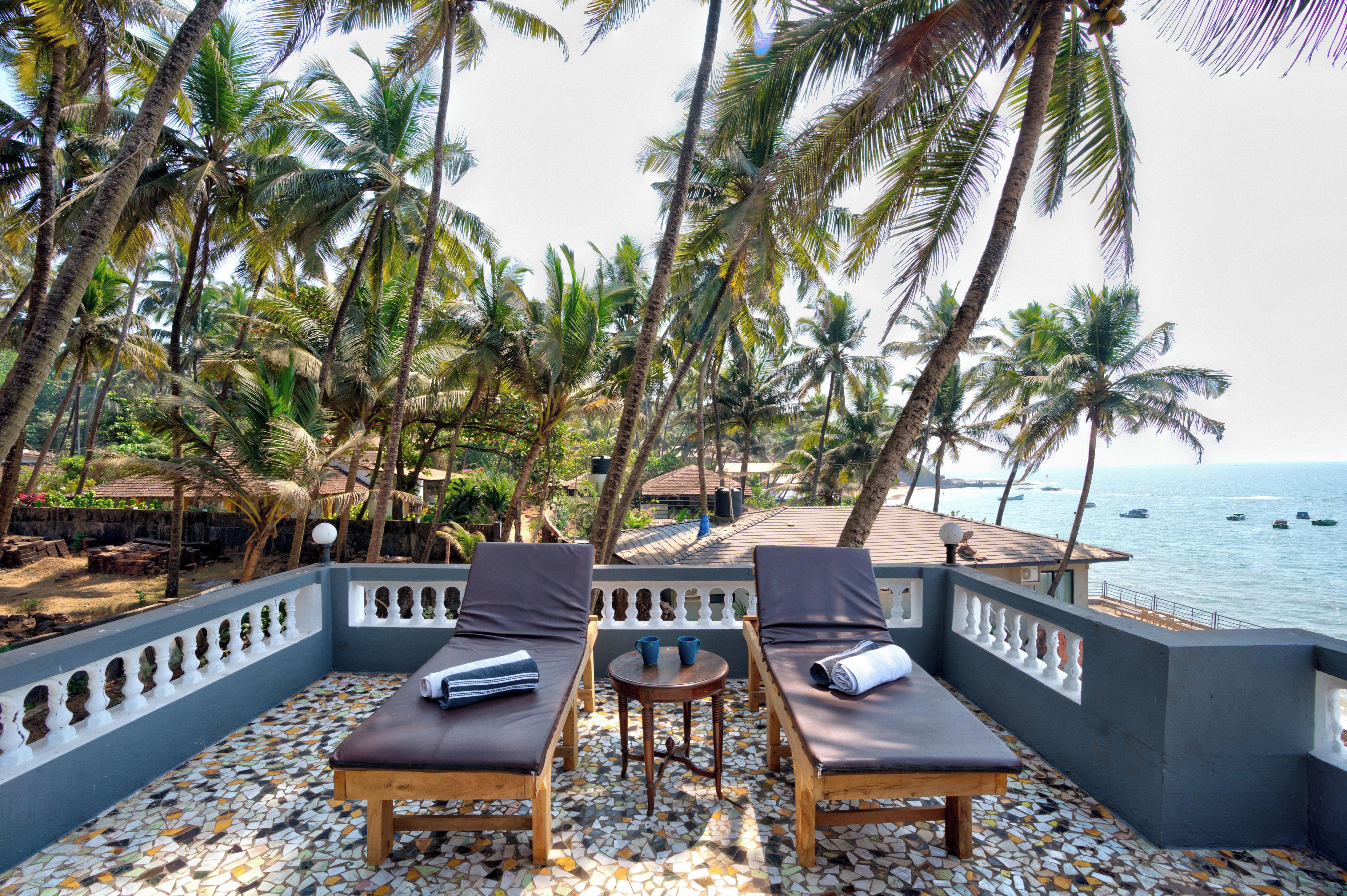 A terrace with two lounge chairs, a small table, and a view of the sea with boats.