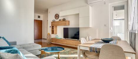 Una sala de estar moderna con sofá, mesa de centro, televisor y comedor con sillas y mesa.