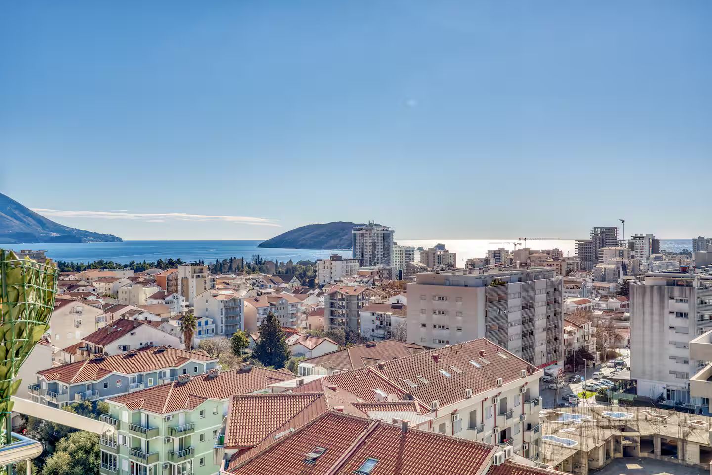A coastal cityscape with a mix of residential and commercial buildings, a clear blue sky, and a view of the sea.